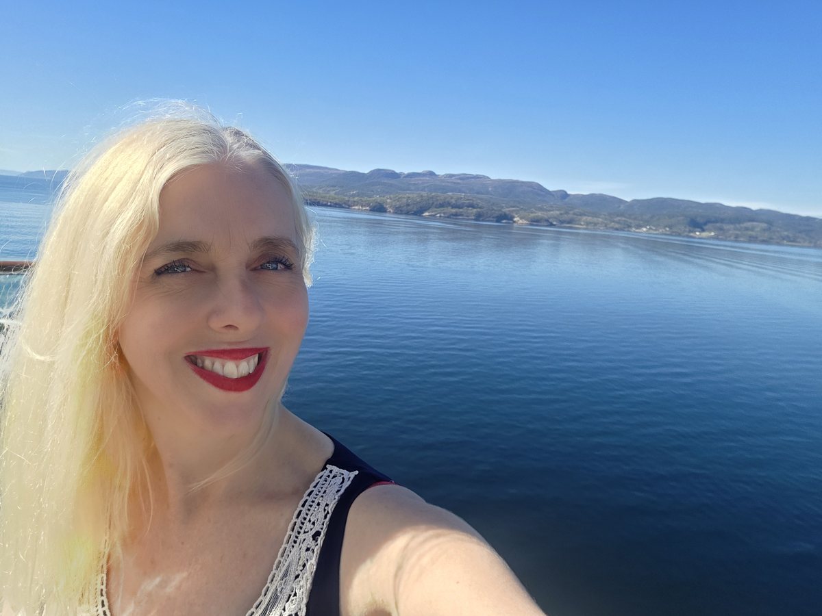 Jo Sehgal smiling on deck, a calm fjord and Norwegian hills behind her
