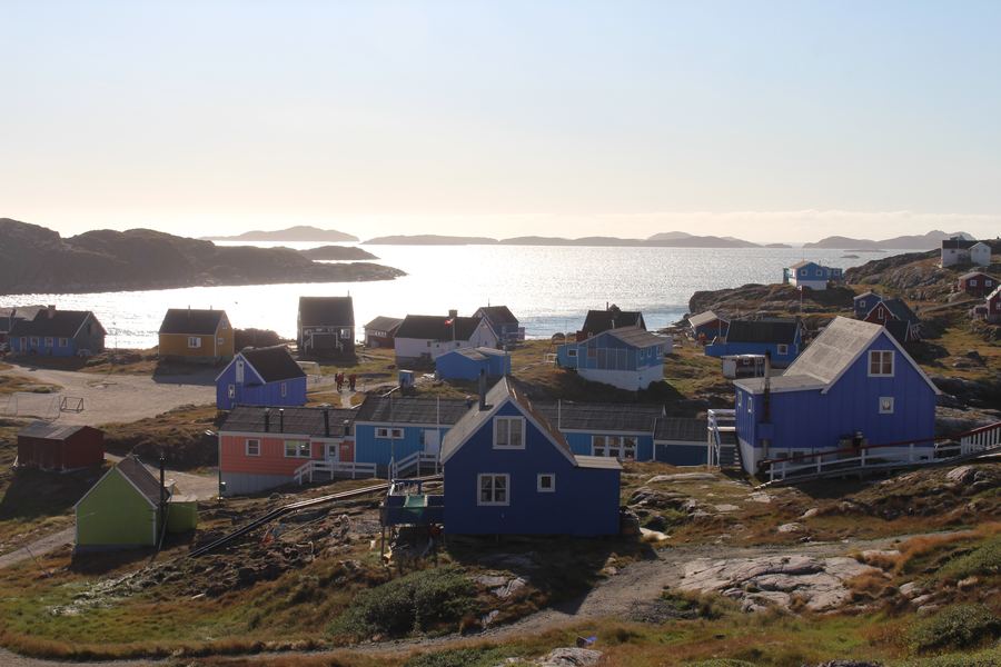 Colourful Arctic village houses along a calm waterfront under soft evening light.