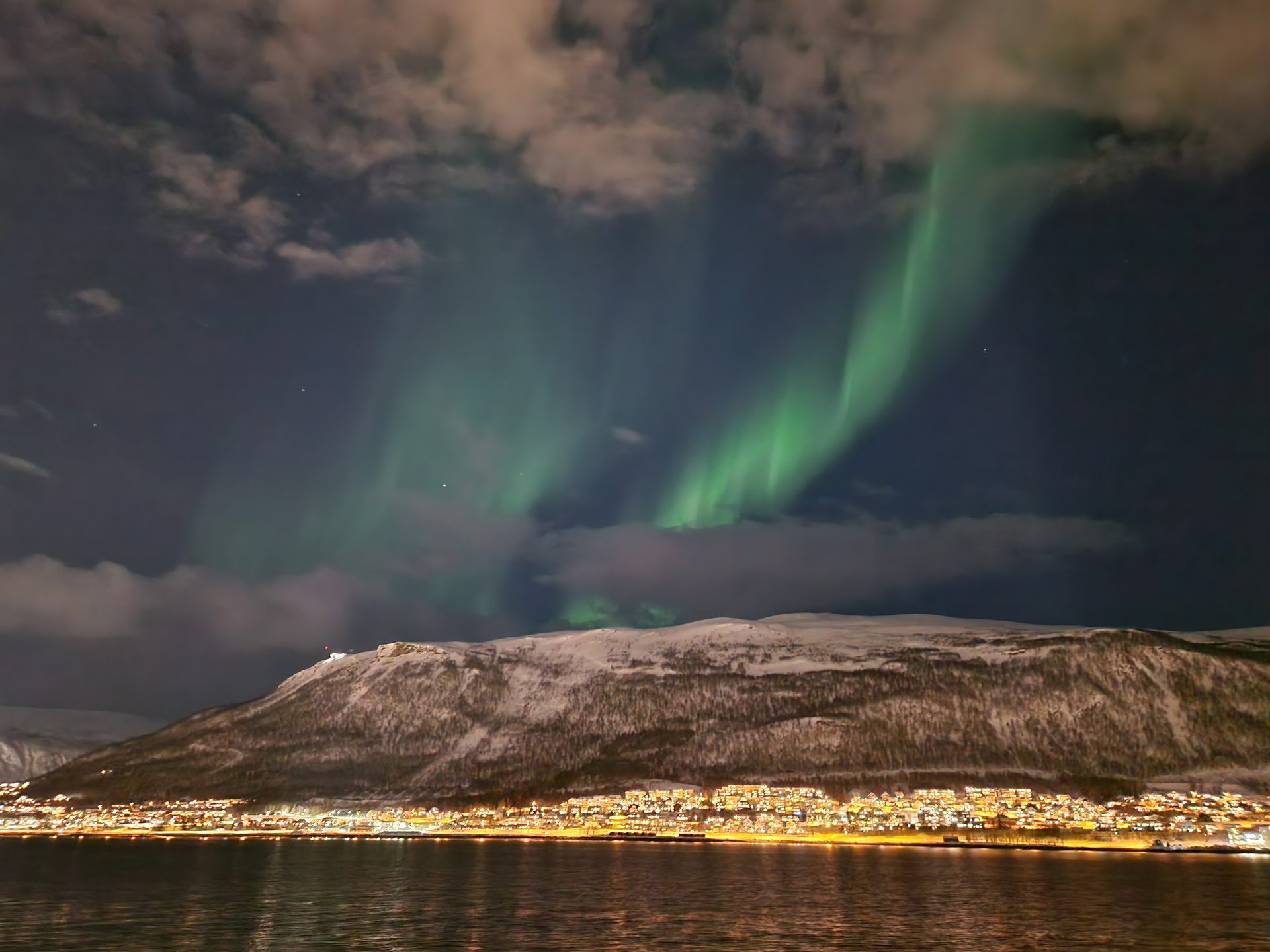 Green aurora over a calm fjord at dusk.