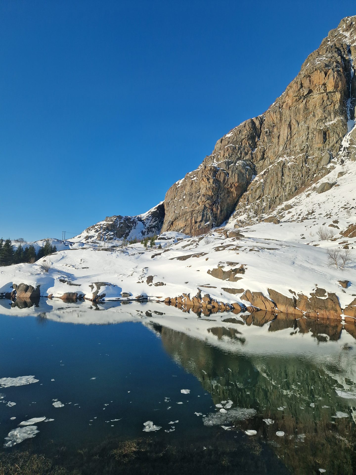 A steep snow-streaked winter peak rising above still water under a clear cold sky.