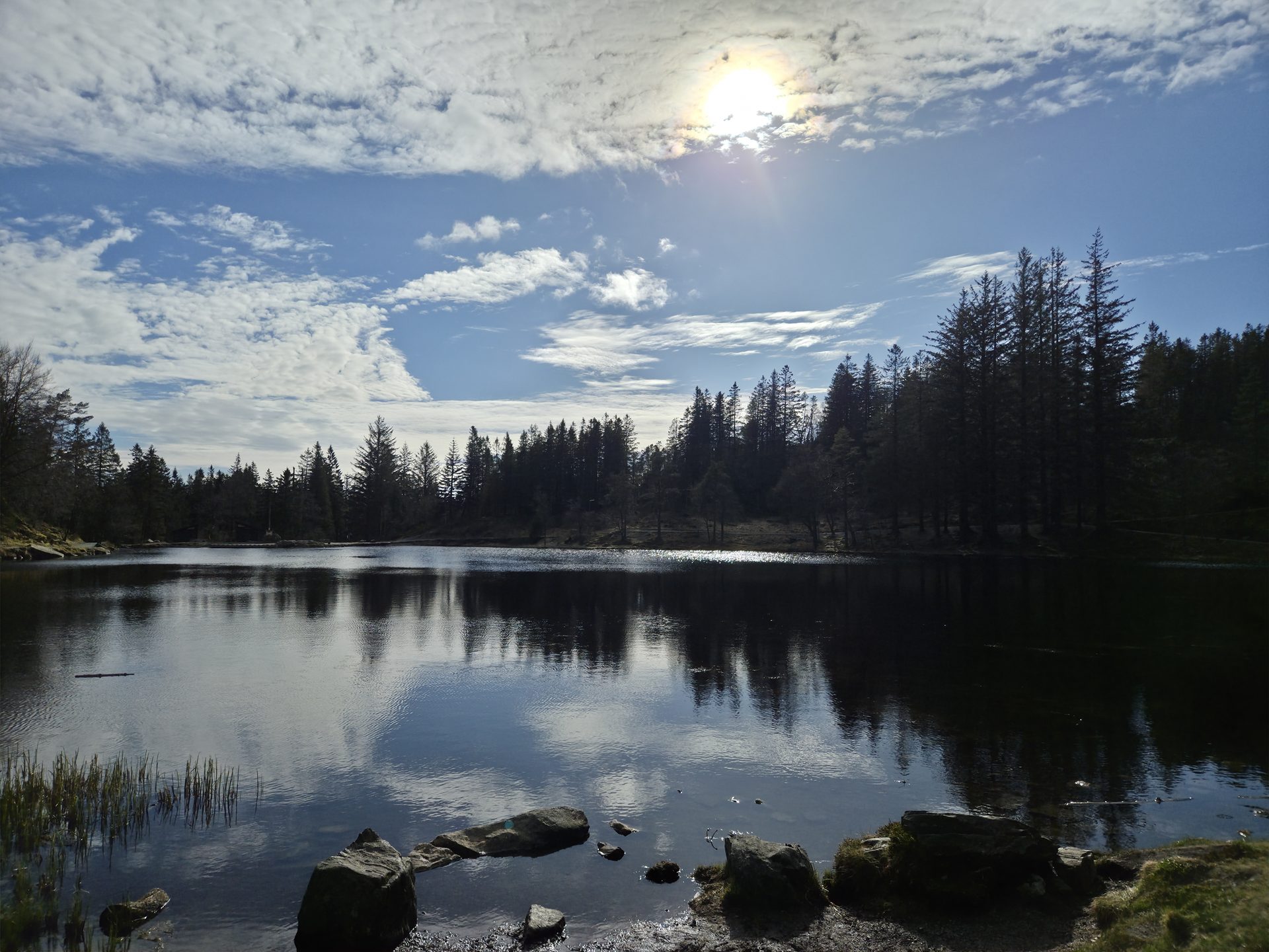 Low golden sun over a glassy, clear-skied fjord with mountains mirrored in still water.