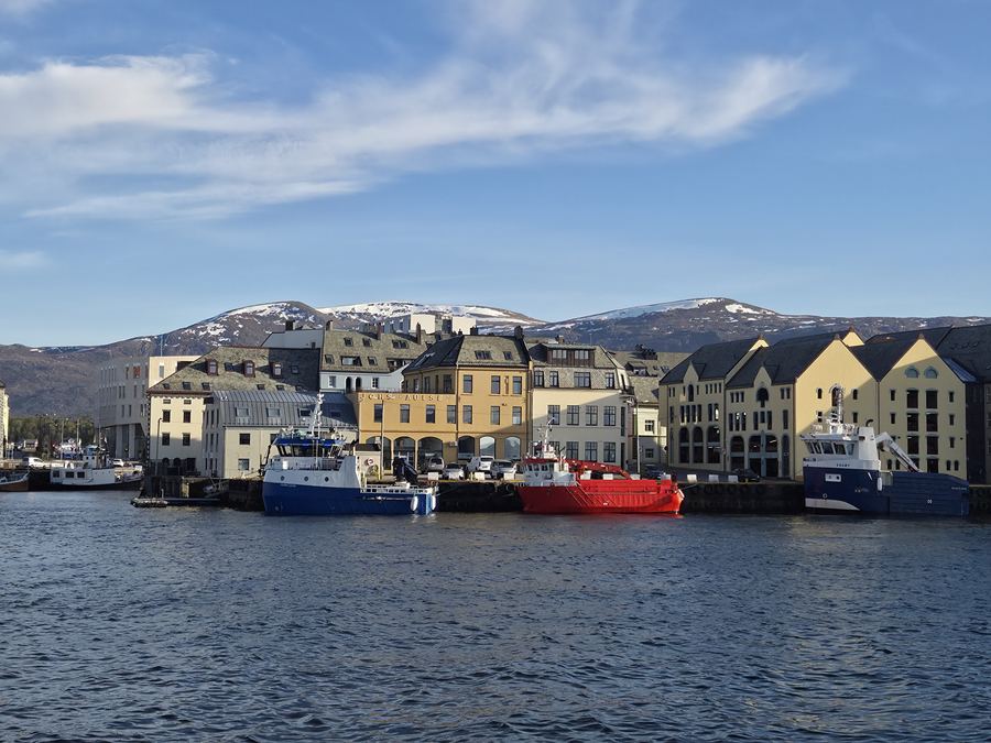 Colourful waterfront buildings reflected in a calm harbour below low green hills.