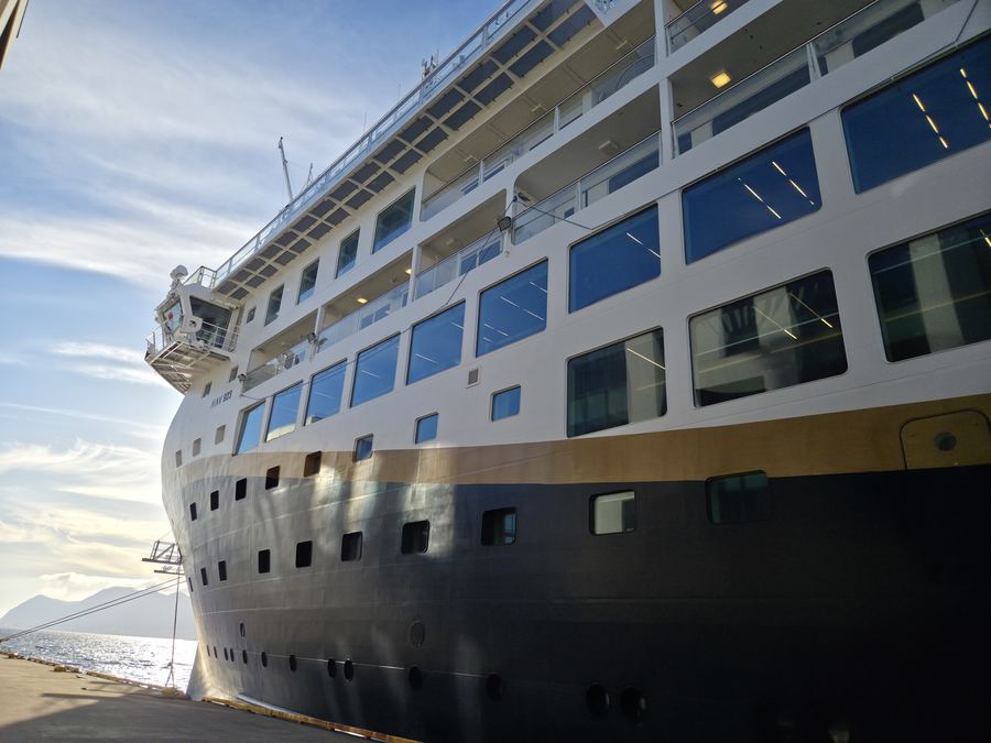 A white coastal cruise ship moored at a quay on a calm fjord.