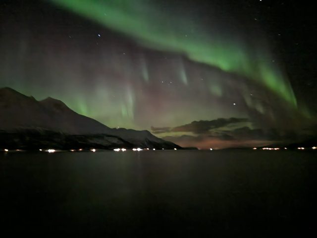 Green and faint-red aurora banding above snow-dusted mountains mirrored in a still fjord.