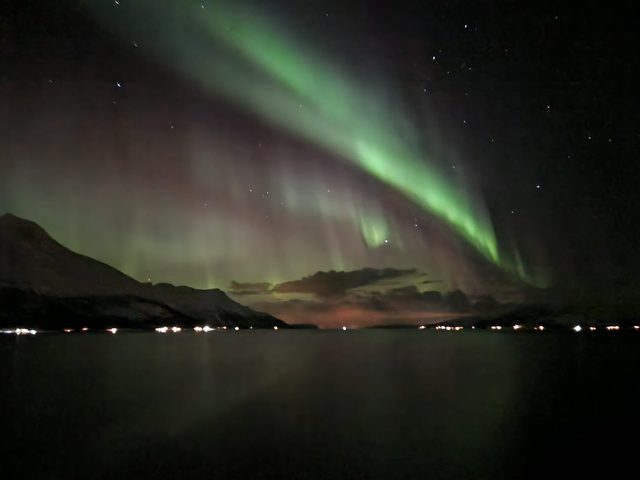 Green aurora sweeping in a long ribbon over the mountains around a Norwegian fjord.