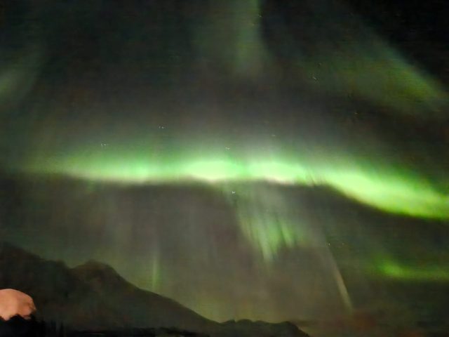 A vivid green aurora curtain folding over dark Arctic mountains.