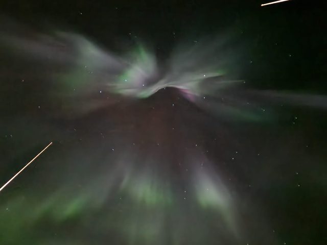 An aurora corona bursting overhead in pale green and violet, rays radiating from directly above.