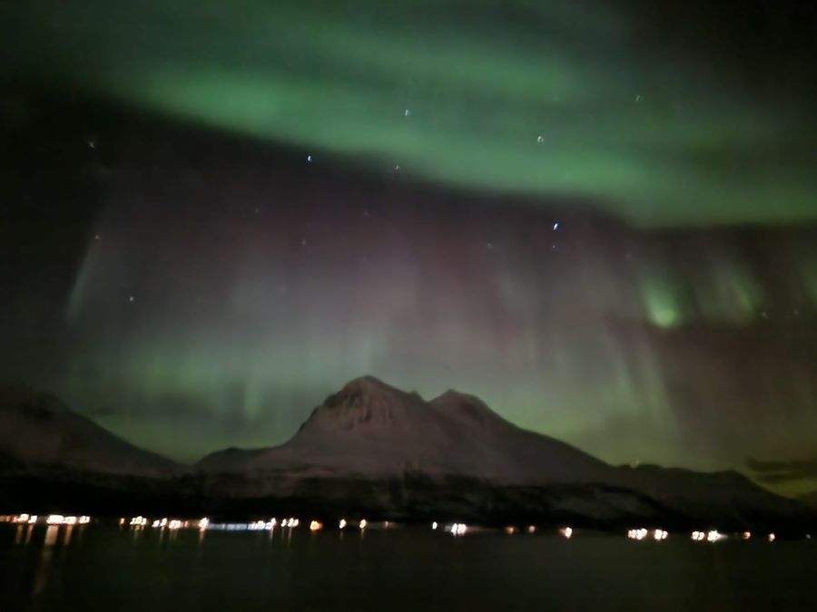 Green aurora glowing above a sharp mountain peak across a dark fjord.