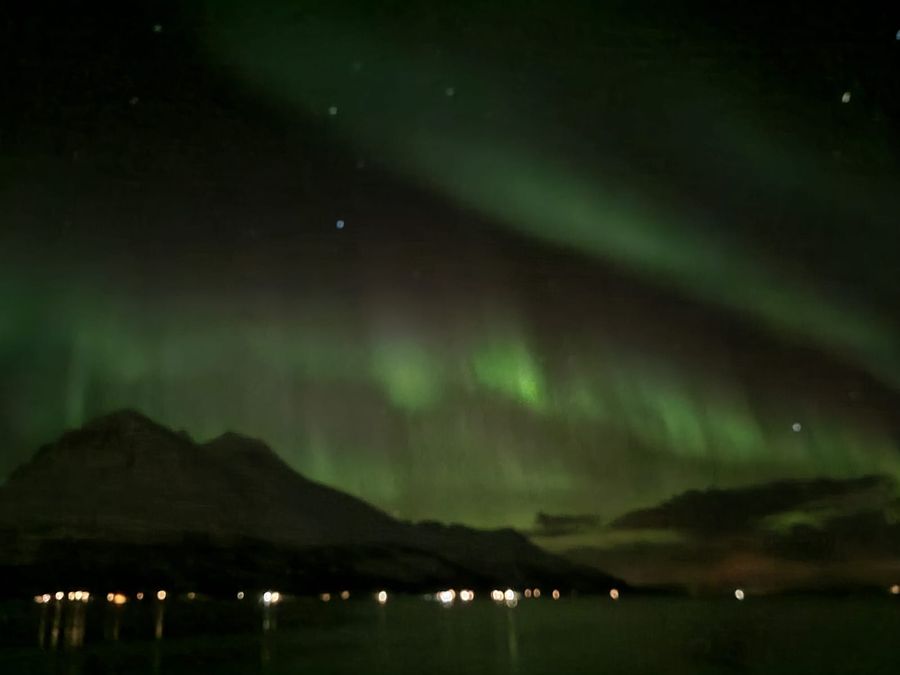 Green aurora over a pointed mountain and a calm fjord under a starry sky.