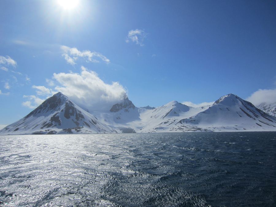 Low Arctic sun over a Svalbard fjord with floating sea ice and snow-streaked mountains.
