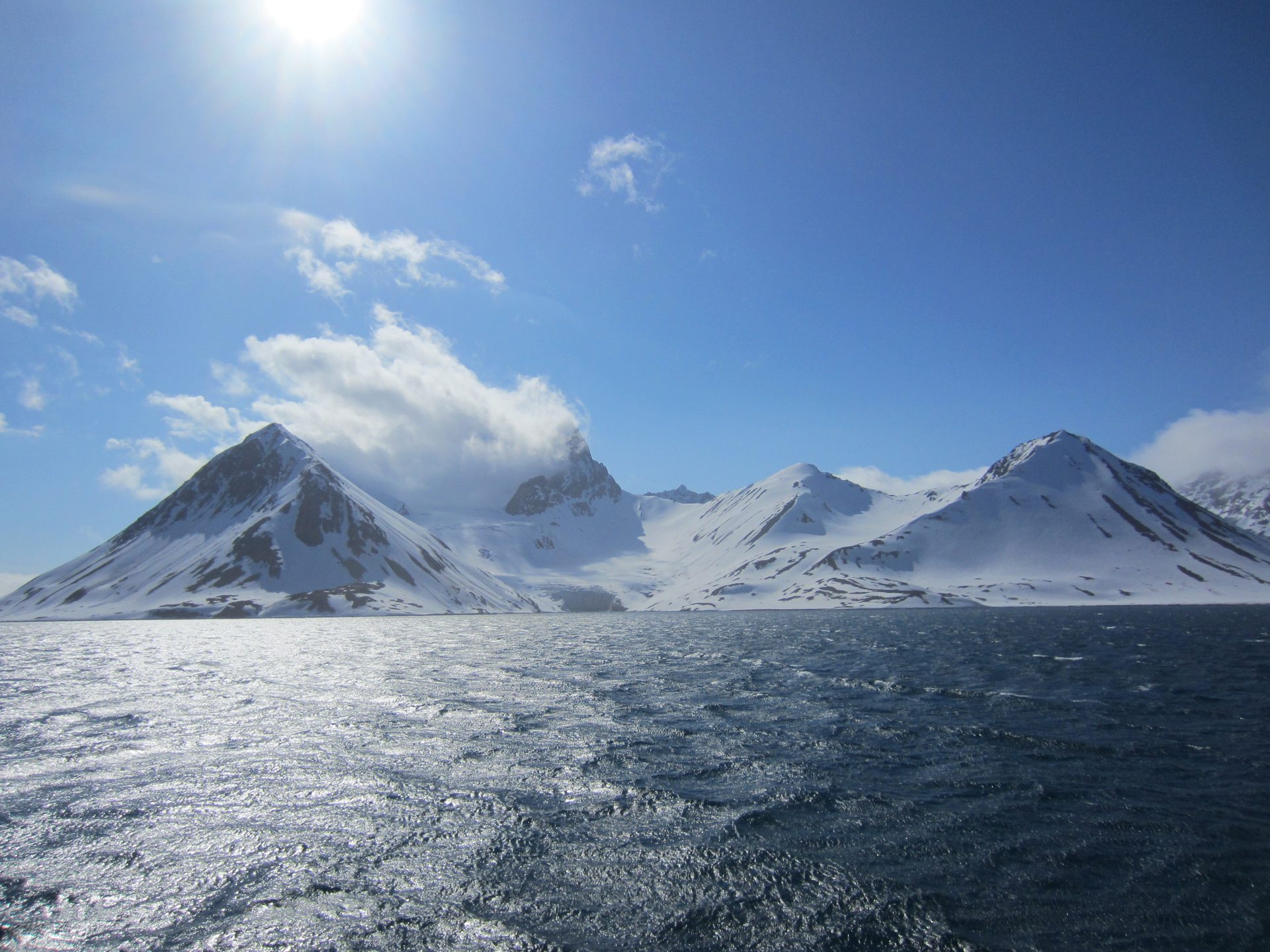 Low Arctic sun over a Svalbard fjord with floating sea ice and snow-streaked mountains.